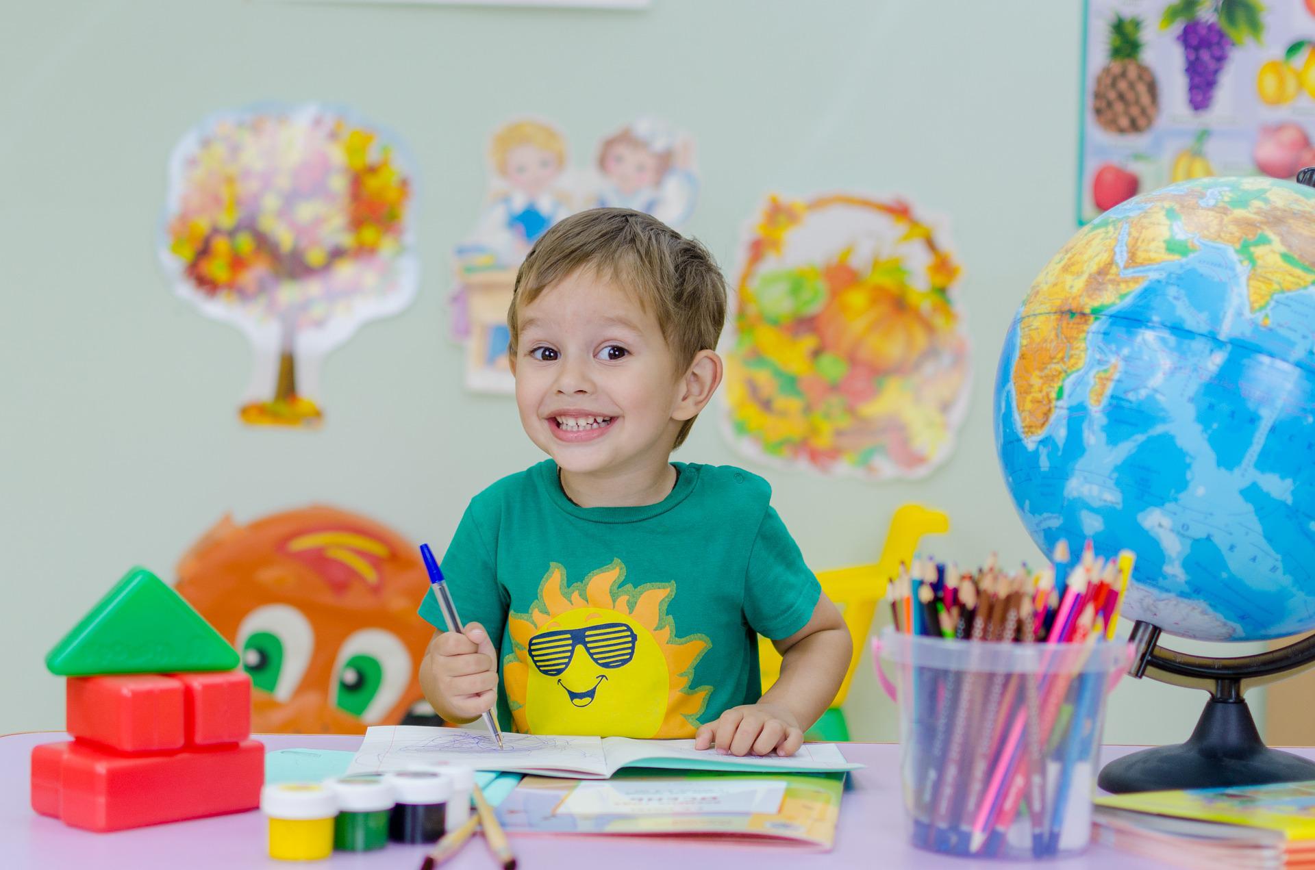 enfant qui fait des gribouillis sur un cahier avec un sourire espiègle