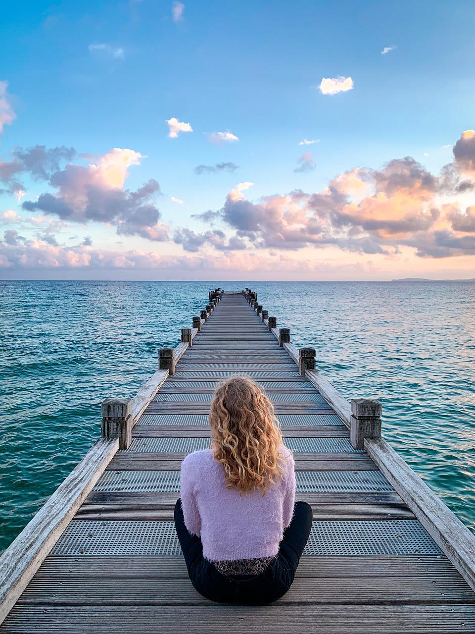 femme assise sur un ponton regardant l'horizon